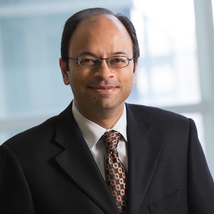 Professional man wearing glasses and dark suit with patterned tie, smiling at camera