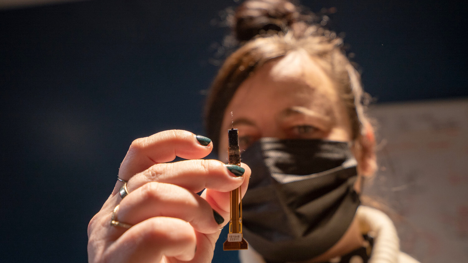 Woman holding a small electronic circuit board component close to camera