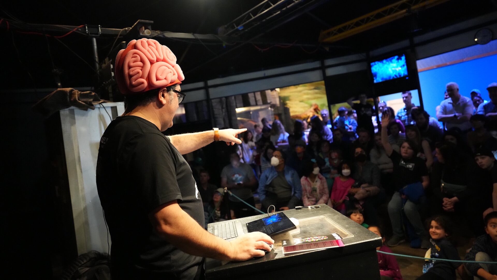 Man wearing oversized brain hat gives presentation to audience at event