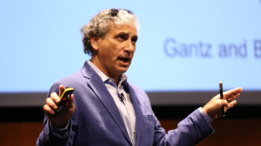 Man in purple jacket speaking at presentation with microphone on stage