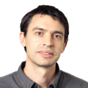 Professional headshot of a man with dark hair wearing gray shirt