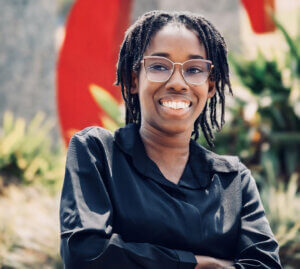 Smiling woman with glasses and dreadlocks wearing black shirt outdoors