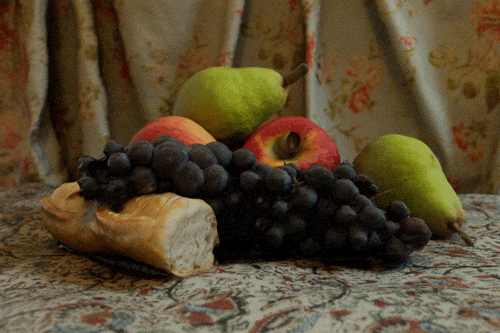 Still life composition with bread, black grapes, red apples, and green pears on patterned fabric.