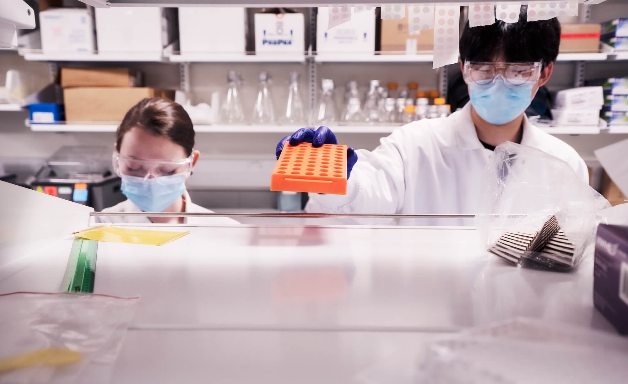 Laboratory scientists in protective gear working with samples and equipment in a research setting.
