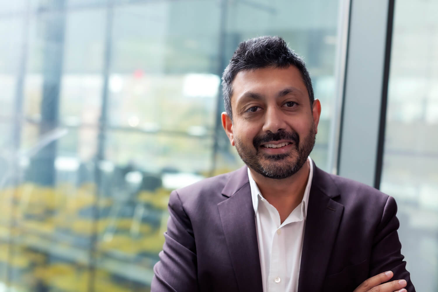 Smiling businessman in purple blazer by high-rise window overlooking city skyline
