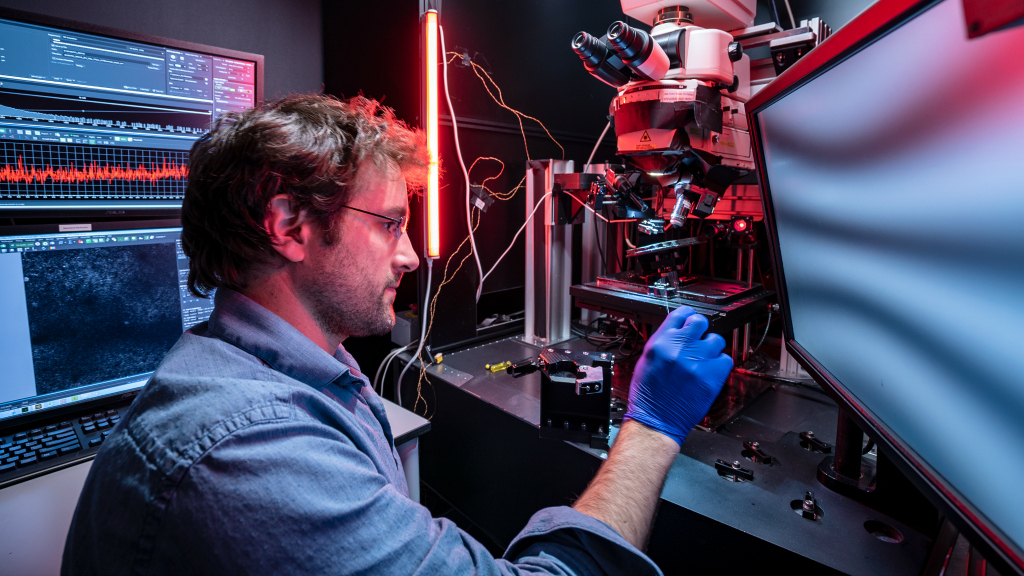 Engineer in blue gloves working on 3D printer with red neon light and computer displays