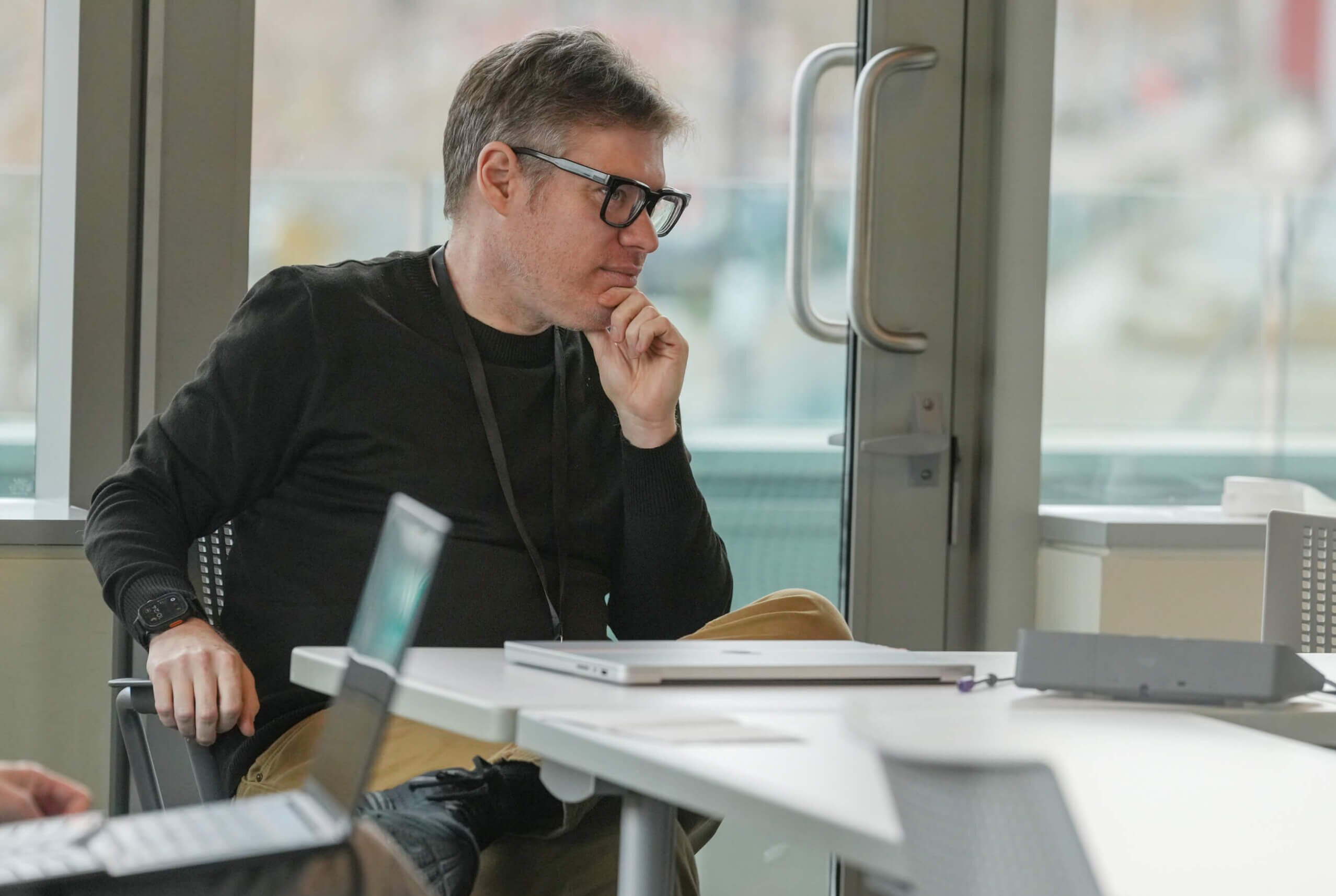 Man in glasses thoughtfully working at desk with ocean view window behind him