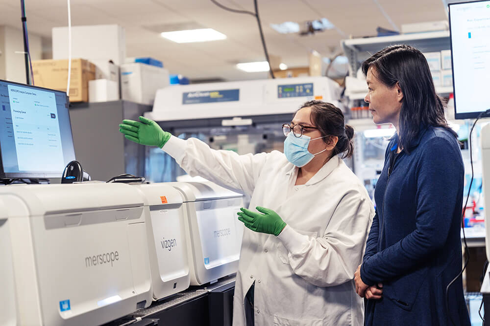 Two scientists in lab coats discussing analysis results near medical diagnostic equipment.