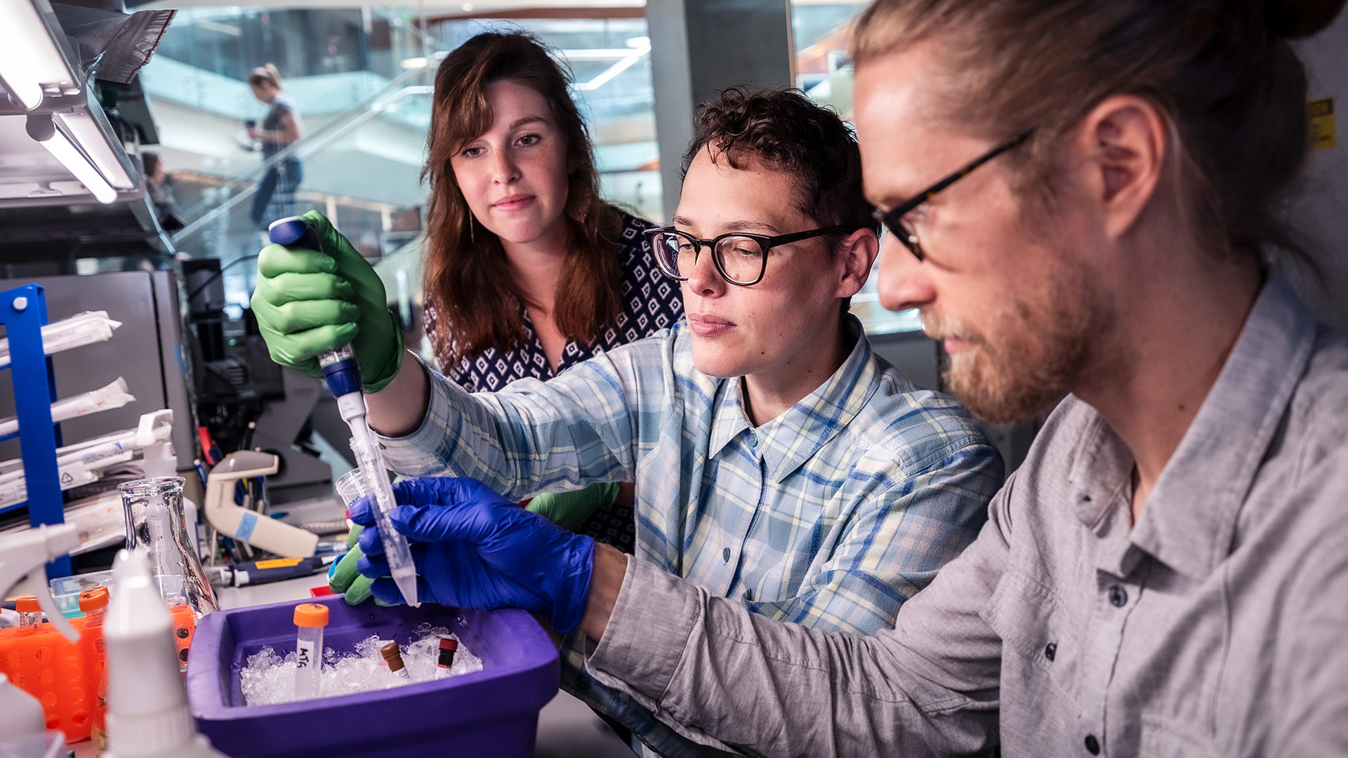 Three scientists in lab conducting DNA or chemical research with pipettes and samples