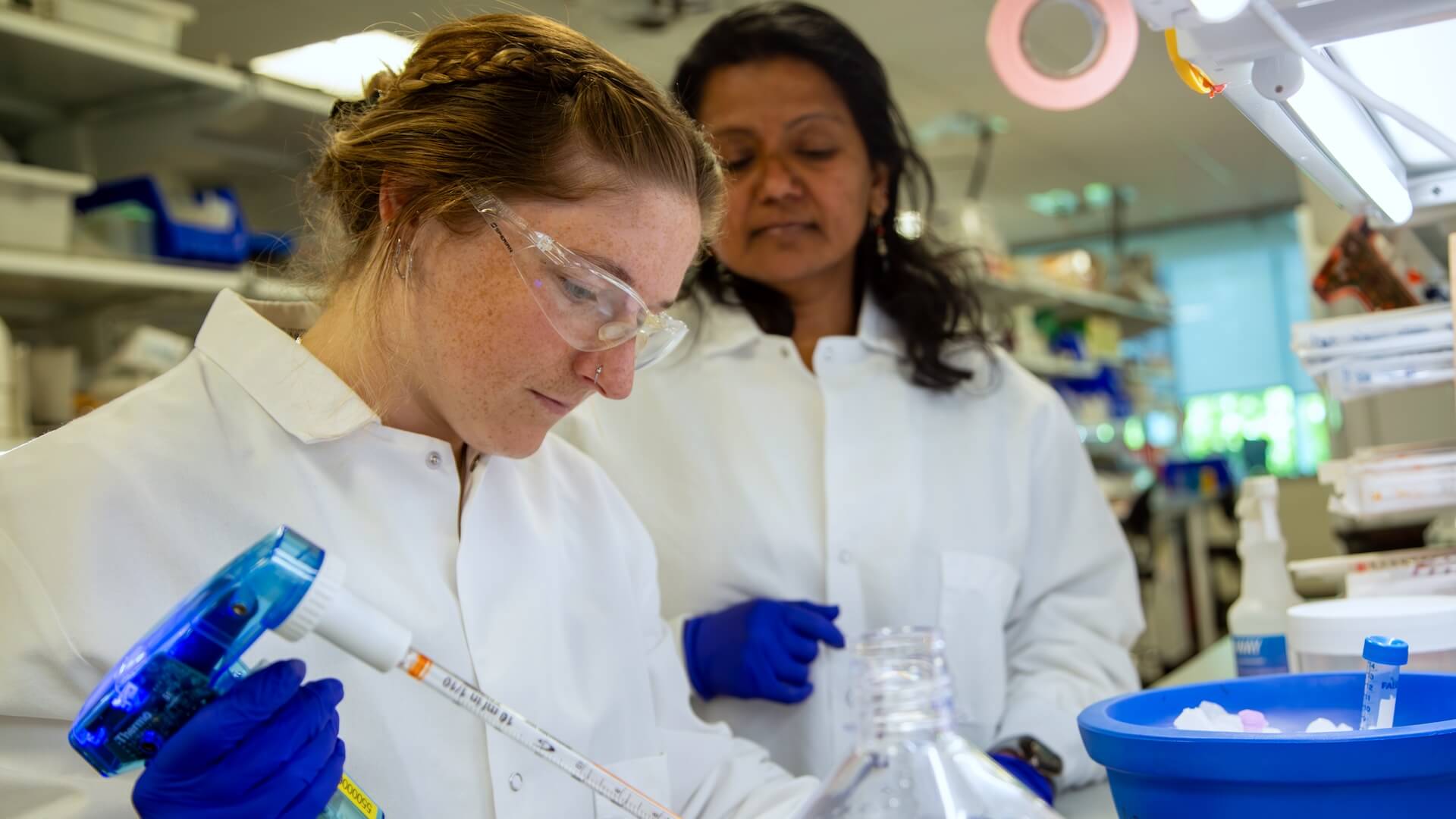 Two scientists in lab coats working with pipette and sample containers in laboratory.