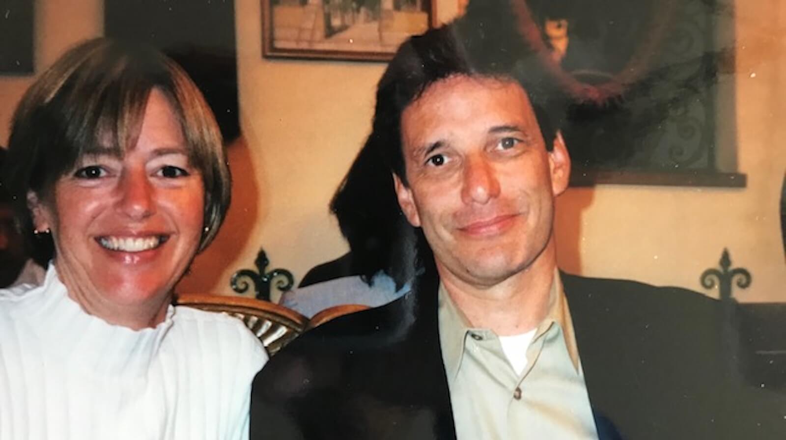 Two people smiling at an indoor gathering with warm beige walls