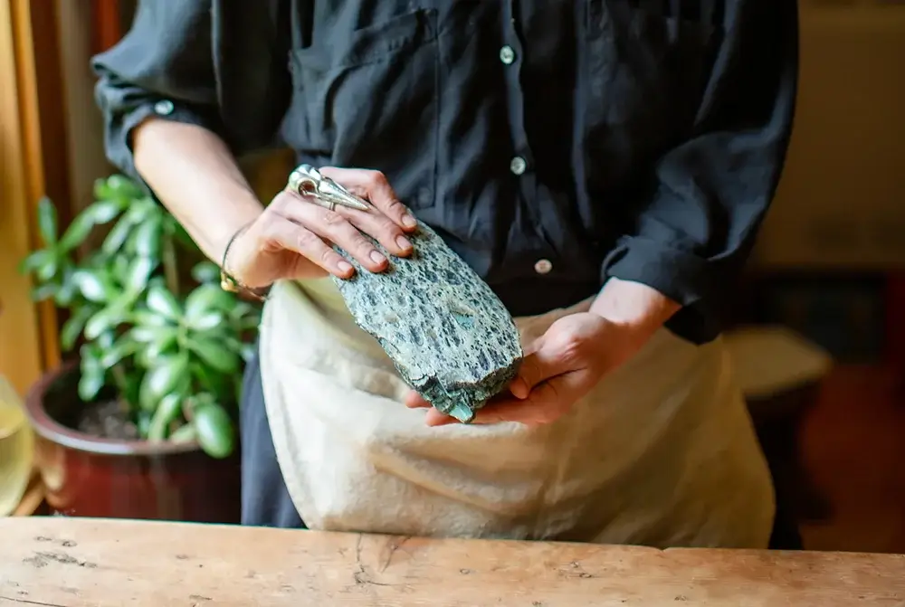 Person in black shirt holding textured gray stone or craft material indoors near plant