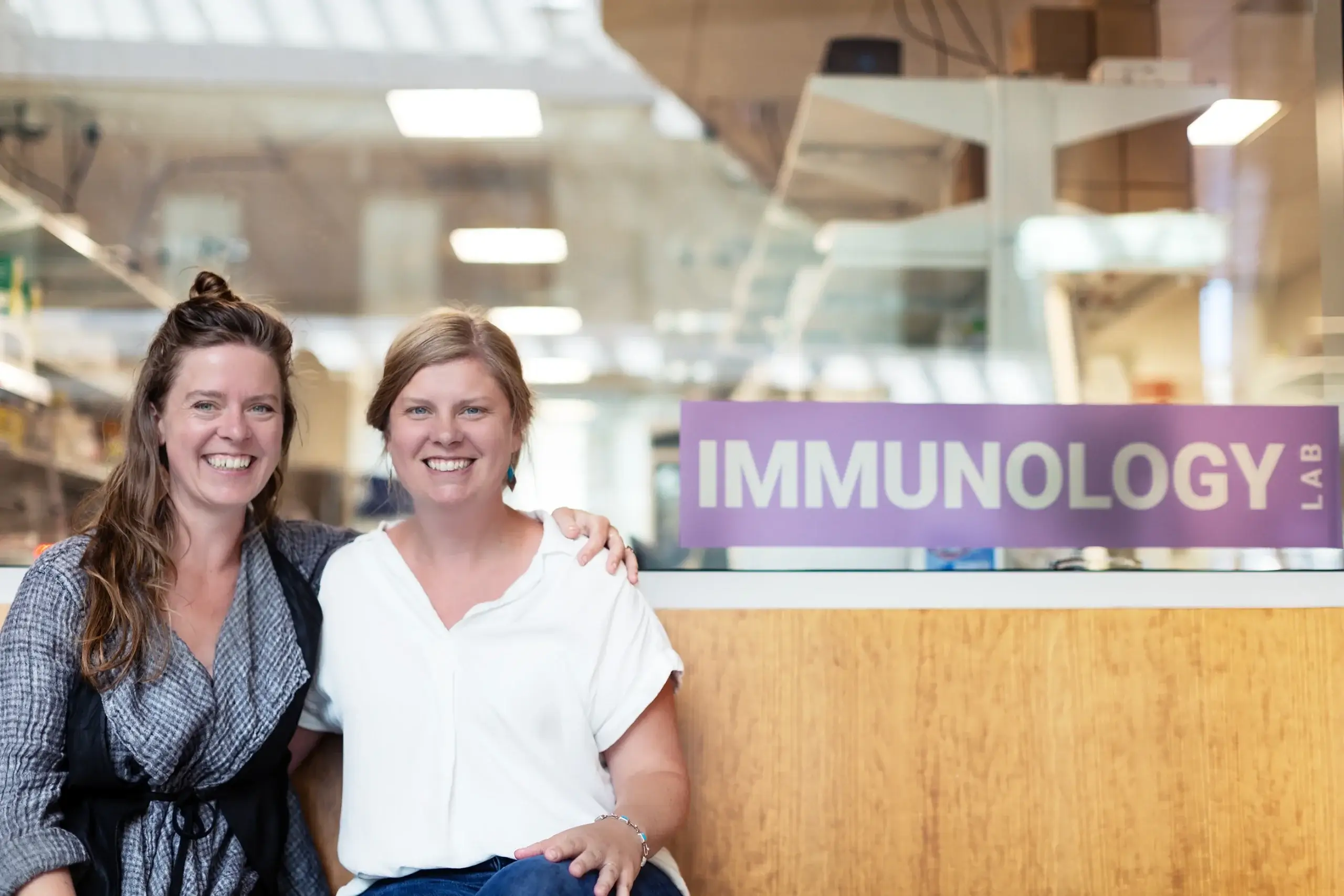 Two smiling women at Immunology Lab reception desk in modern research facility