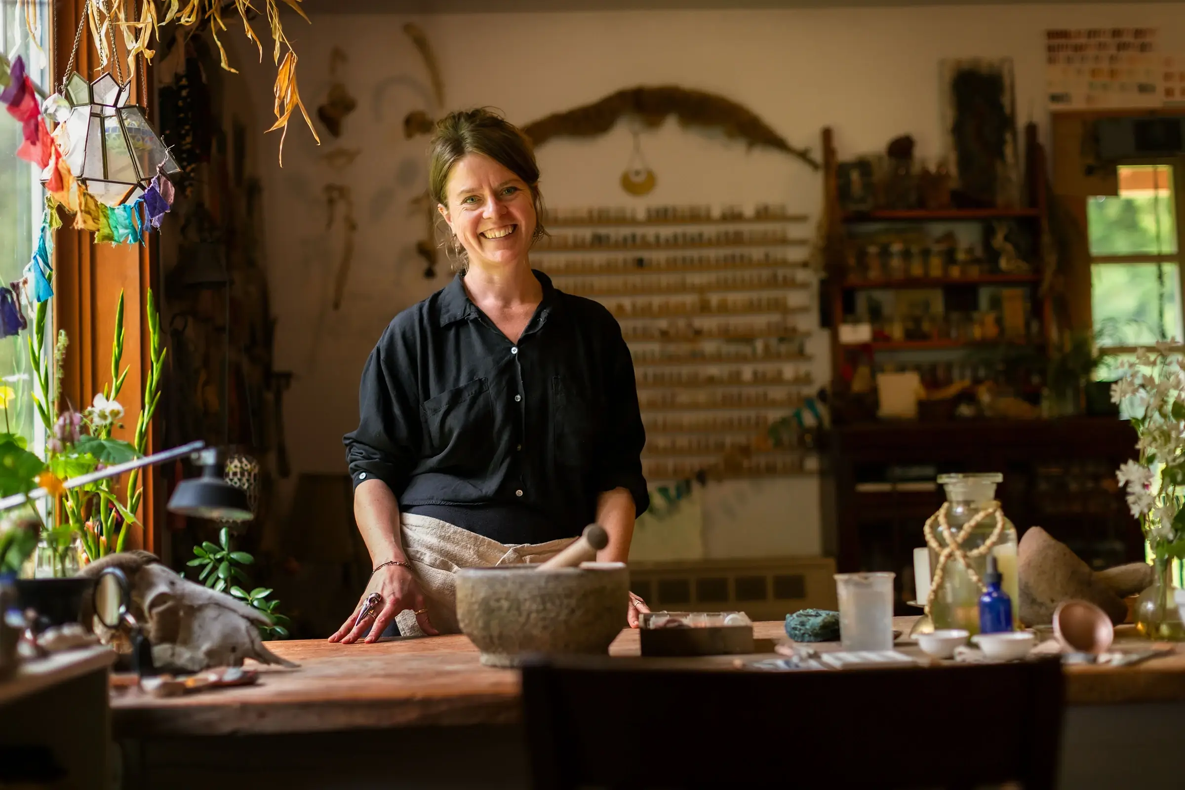Woman smiling at pottery workshop table with clay tools and decorative flowers