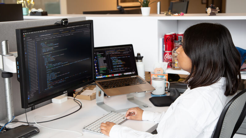 Developer working at desk with dual monitors displaying code and design software.