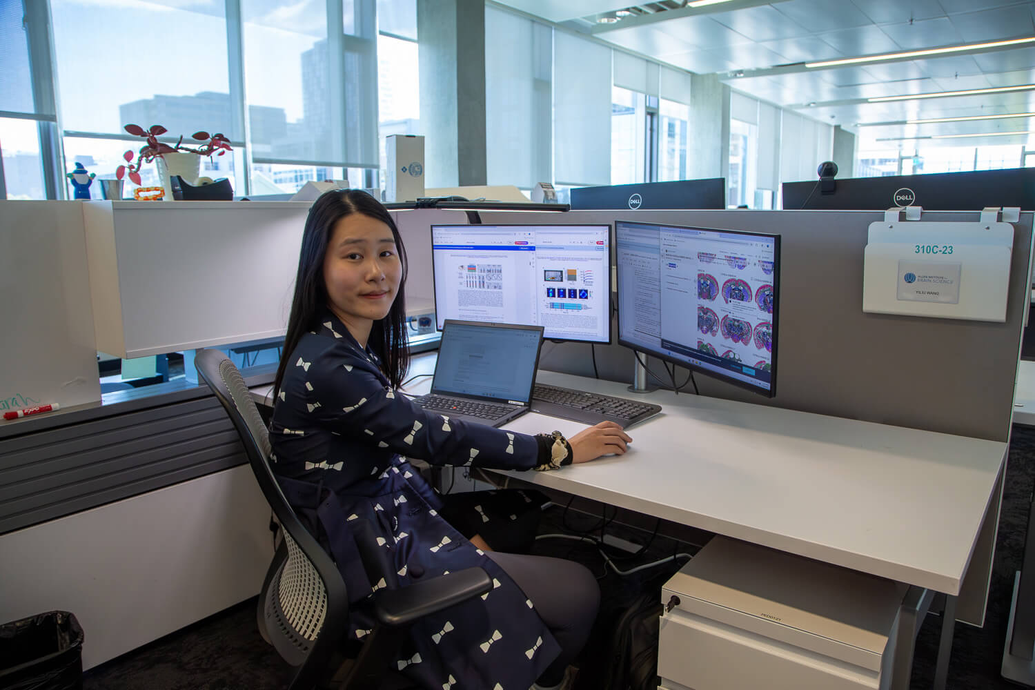 Woman seated at modern office desk with multiple monitors and laptop overlooking city skyline