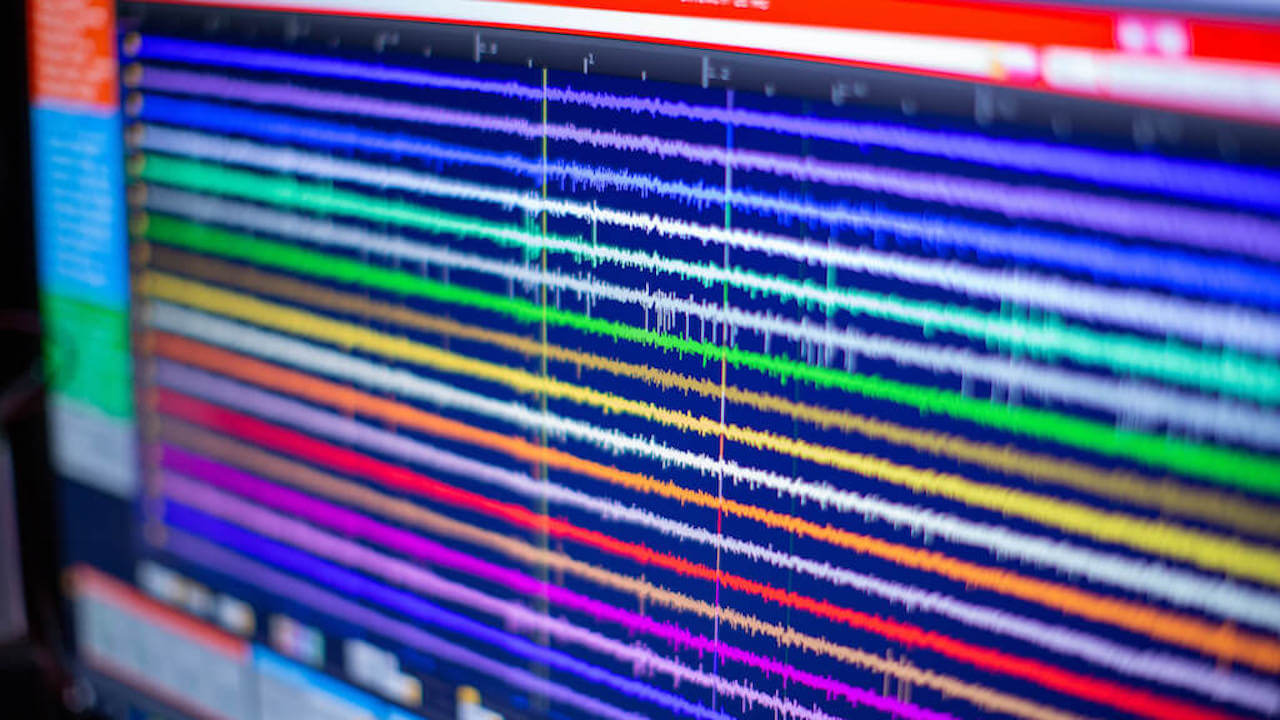 Digital audio waveform editor showing multiple colored audio tracks with vertical playhead indicator.