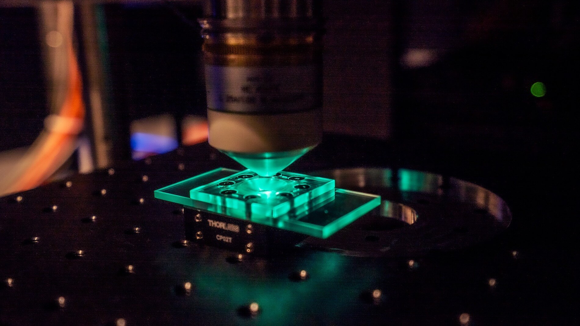 3D printer nozzle depositing glowing green material onto a precision platform at night