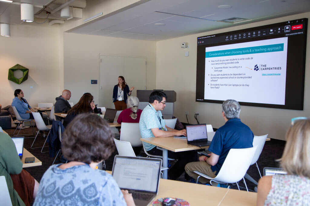 Instructor pointing to a screen with a presentation in a room full of educators.