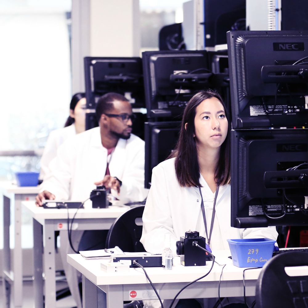 Three researchers sit at electrophysiology rigs.