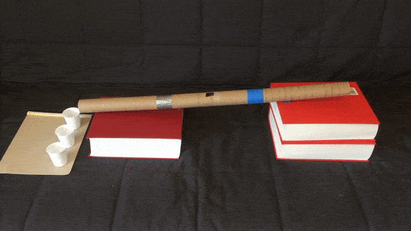 Seesaw toy made with books, wooden stick, and egg carton on dark fabric