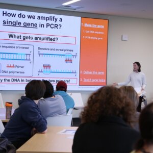 Teacher presenting DNA amplification lecture to students in classroom with projection screen