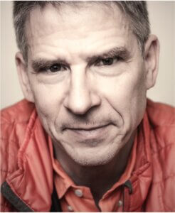 Portrait of a middle-aged man with short gray hair wearing a red jacket.