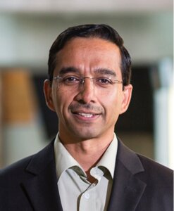 Professional headshot of a man in dark blazer and light shirt smiling indoors.