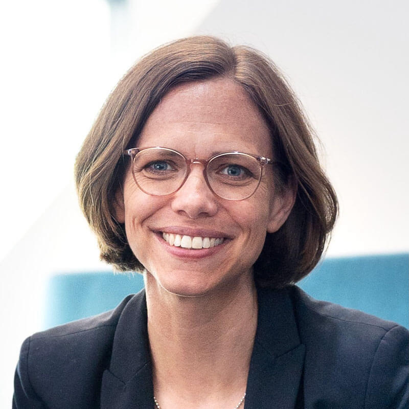 Professional woman with glasses smiling at camera wearing dark blazer