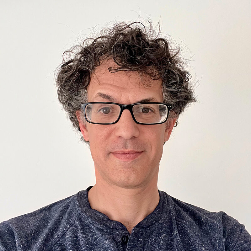 Man with curly gray hair and black glasses wearing dark blue shirt