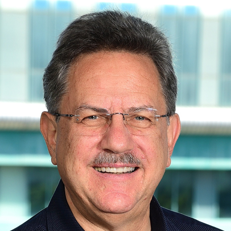 Smiling middle-aged man with gray hair wearing glasses and dark shirt indoors