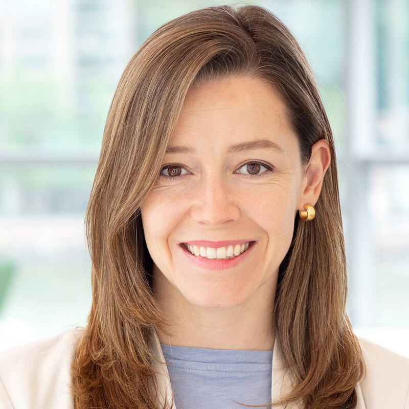 Smiling woman with brown hair wearing gold earrings and blue top