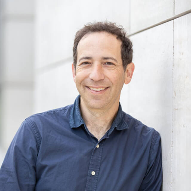 Portrait of a smiling man wearing a dark blue button-up shirt against a white background.