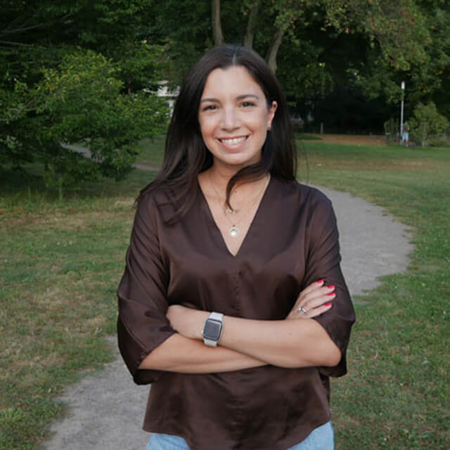 Woman smiling with arms crossed in park wearing brown shirt and smartwatch