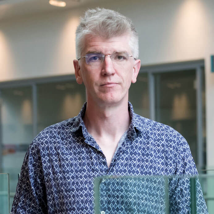 Older man with white hair and glasses wearing a blue patterned shirt in modern interior