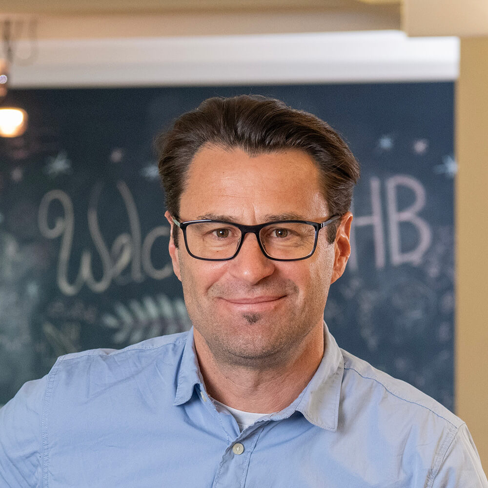 Professional man wearing glasses and light blue shirt indoors, smiling at camera