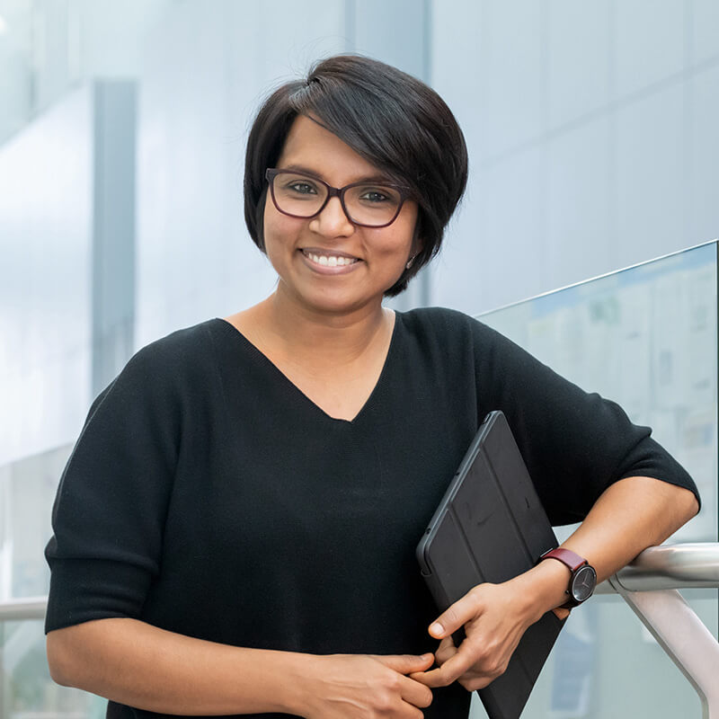 Woman wearing glasses and black shirt holding tablet smiling at camera