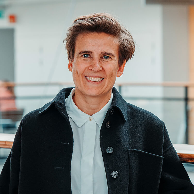 Young man smiling at camera wearing black blazer and white shirt indoors.
