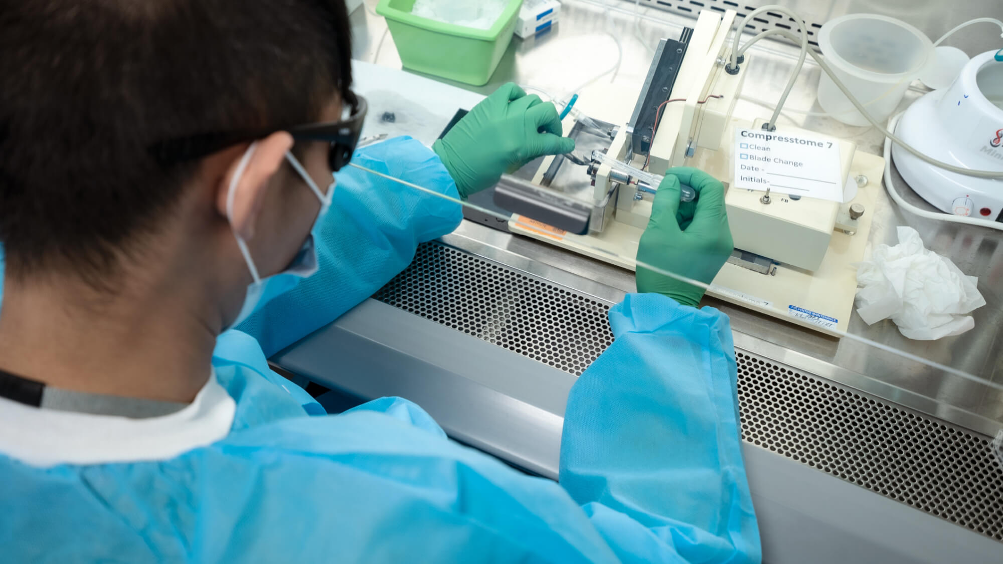 Laboratory technician in protective gear working with sample in biosafety cabinet.