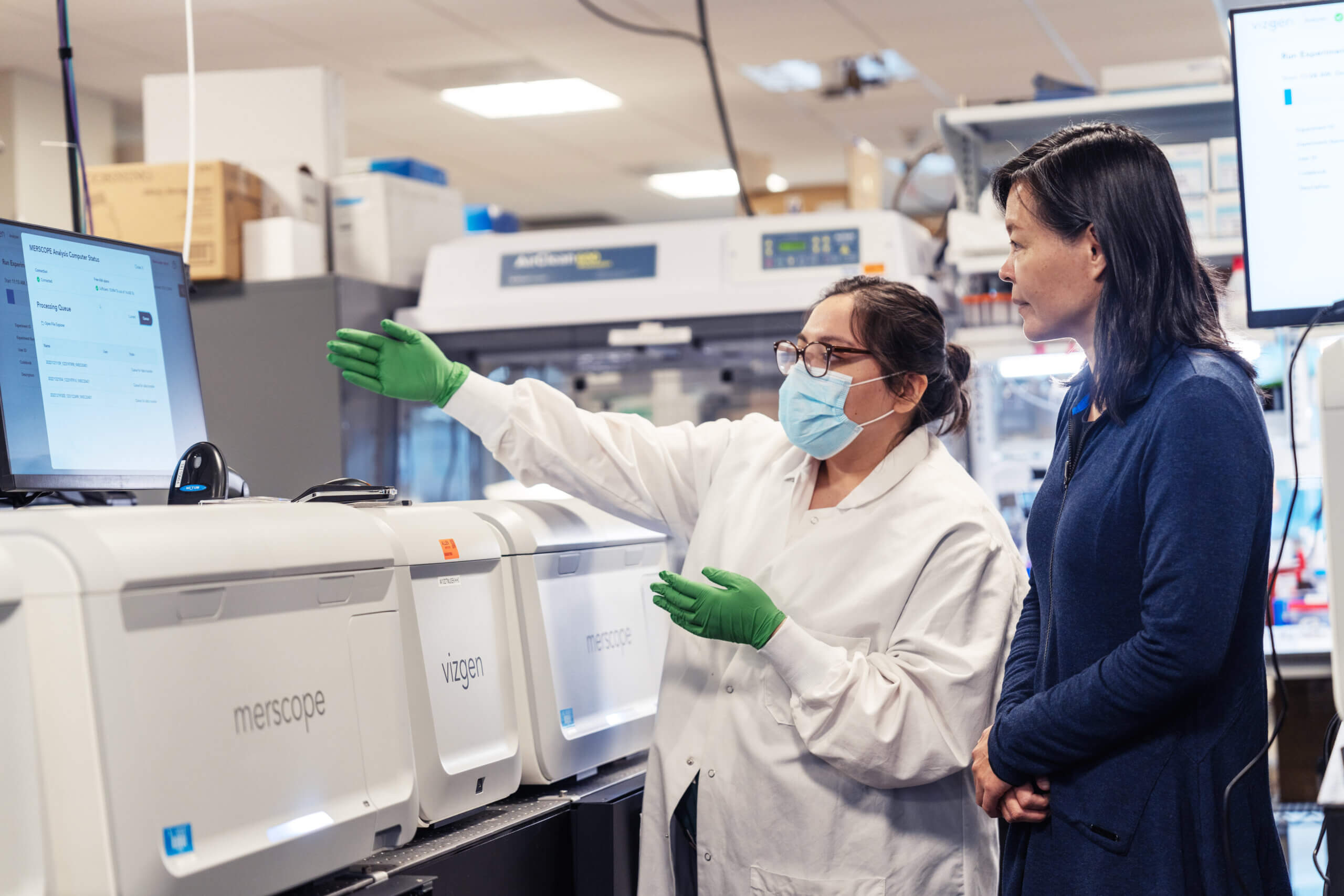 Two scientists in laboratory discussing data at computer near medical diagnostic equipment.