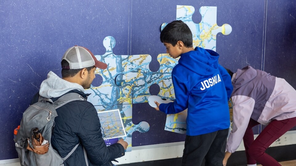 Children solving a colorful map puzzle together on a blue wall during an interactive learning activity.