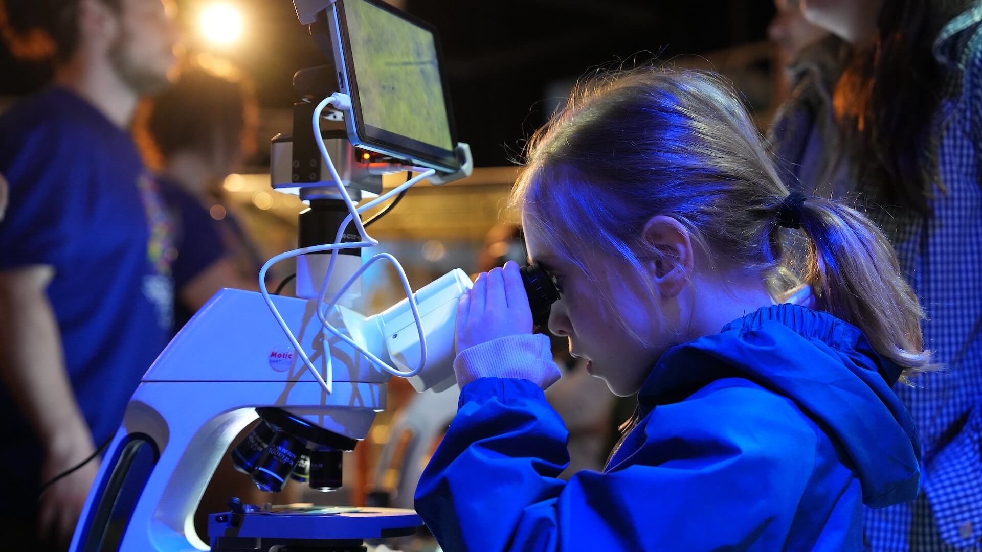 Child examining microscope with monitor display at night science exhibit event