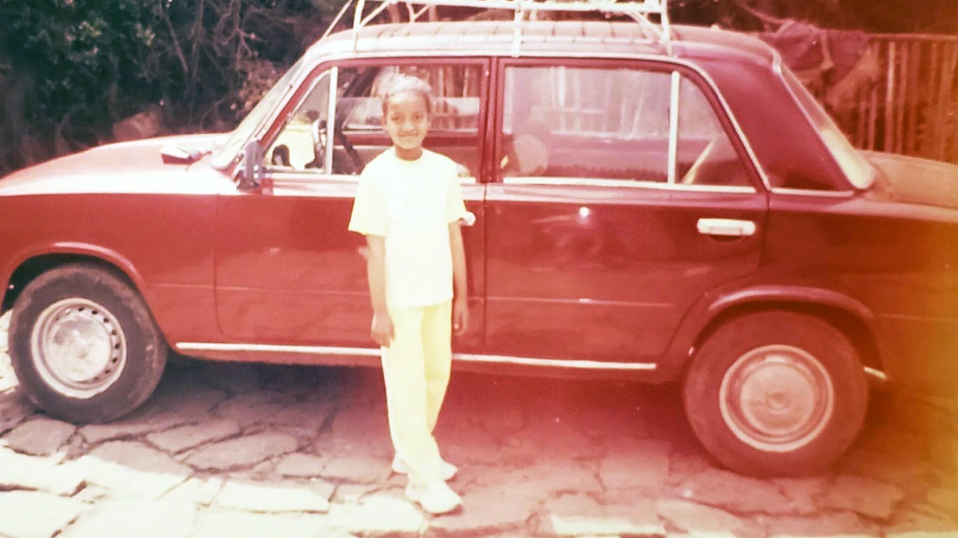Young boy standing in front of red vintage car with open door