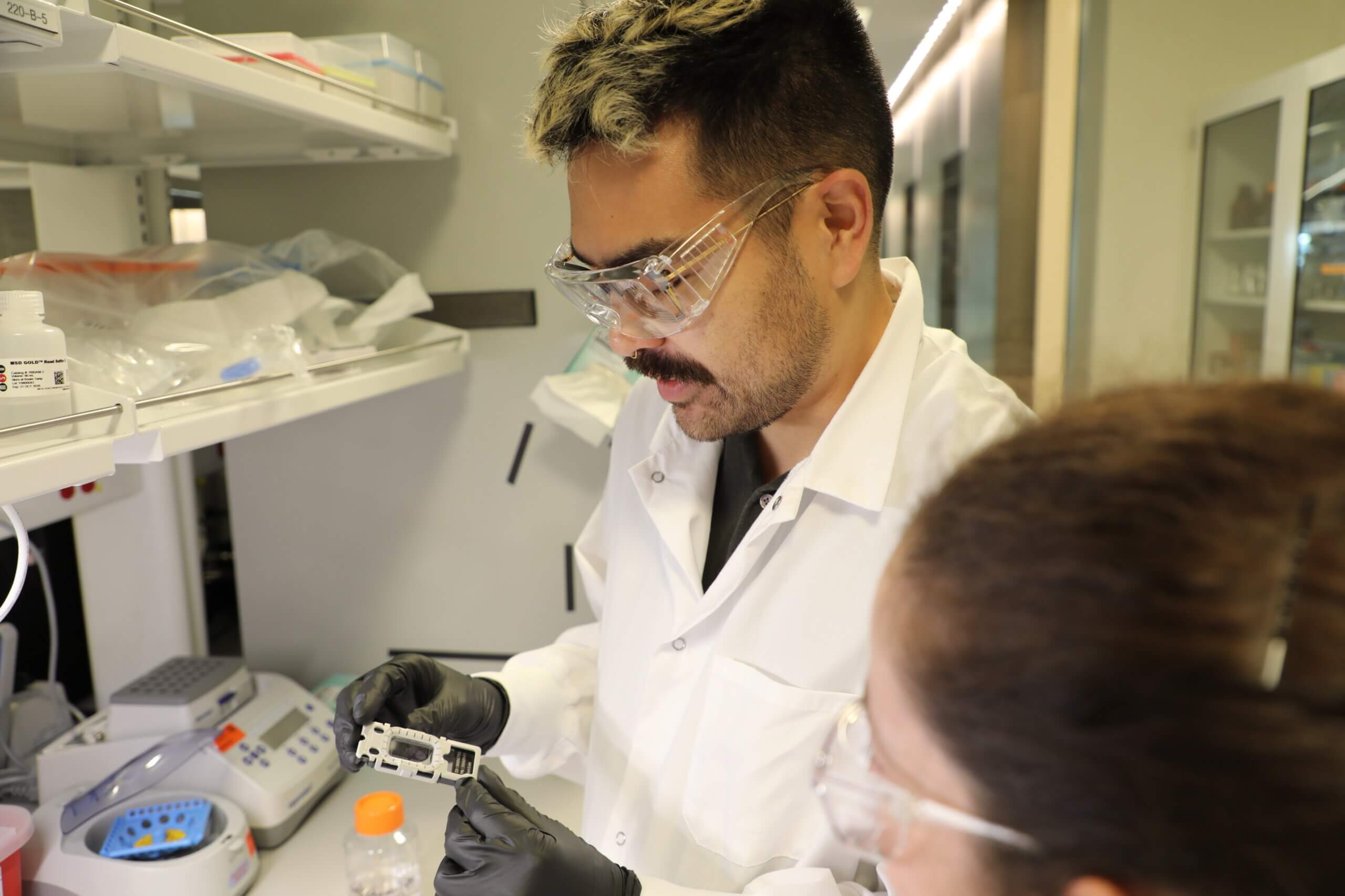 Scientist in lab coat and safety glasses working with laboratory equipment.