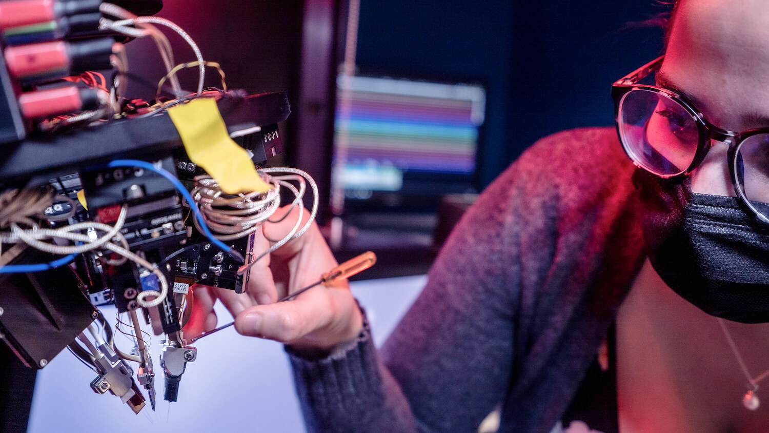 Person assembling electronic circuit board with colorful wires and components under pink lighting