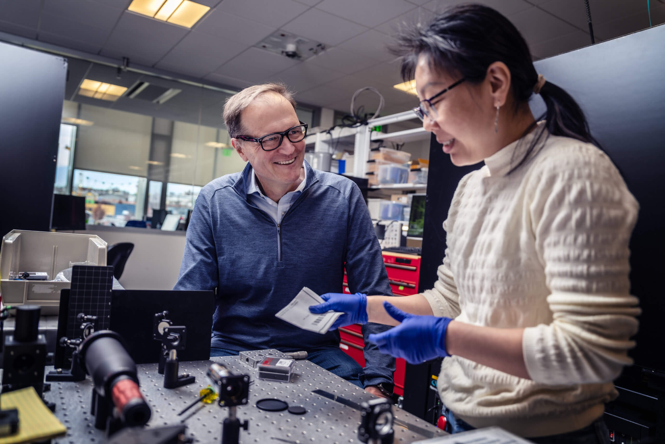 Two scientists collaborating in laboratory with optical equipment and electronic components