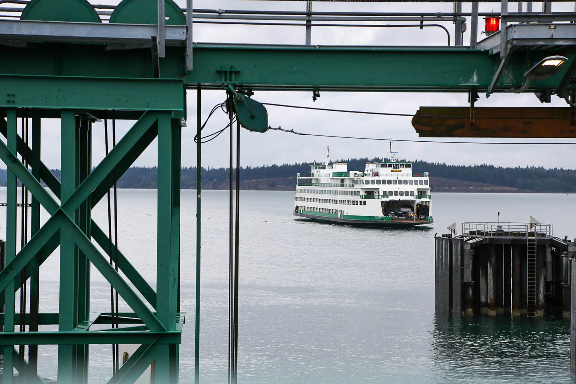 Green and white ferry boat on water viewed through industrial green metal dock structure