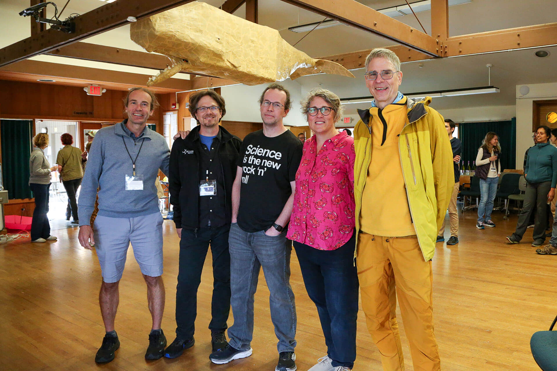 Five people posing together in a gymnasium under a large gold sculpture.