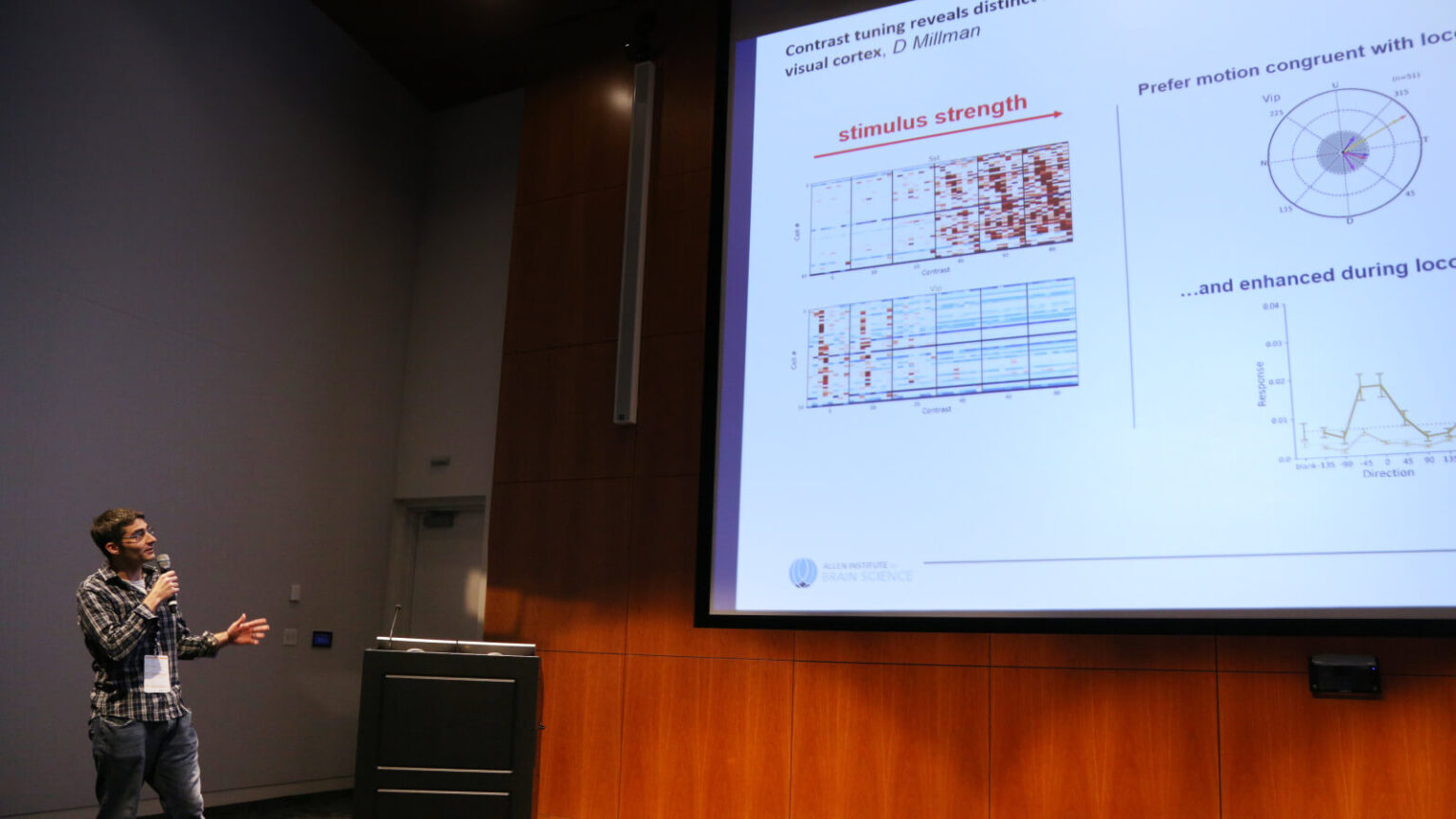 Presenter discussing neuroscience research on visual cortex contrast tuning with data visualizations displayed on screen