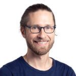 Man with glasses wearing dark blue shirt, smiling at camera